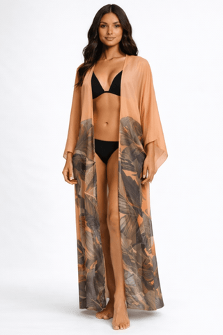 Woman wearing a long kimono-style garment with a tropical leaf pattern over a black bikini on a white background.