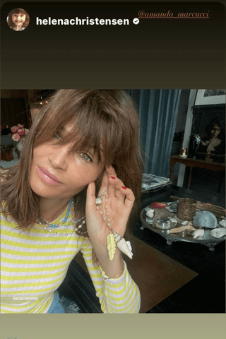 Woman in a yellow and white striped shirt holding a necklace in a room with decor.