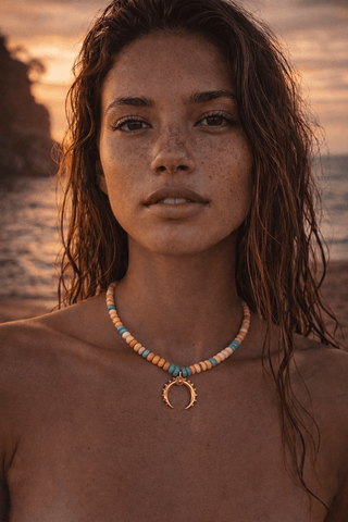 Luxury opal beaded necklace with gold crescent pendant worn by model at sunset, featuring orange, turquoise and ivory beads from Resort 2026 collection