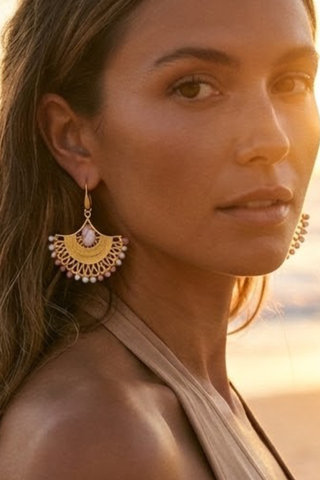 Close-up of a woman wearing large, ornate earrings with a warm, blurred background.
